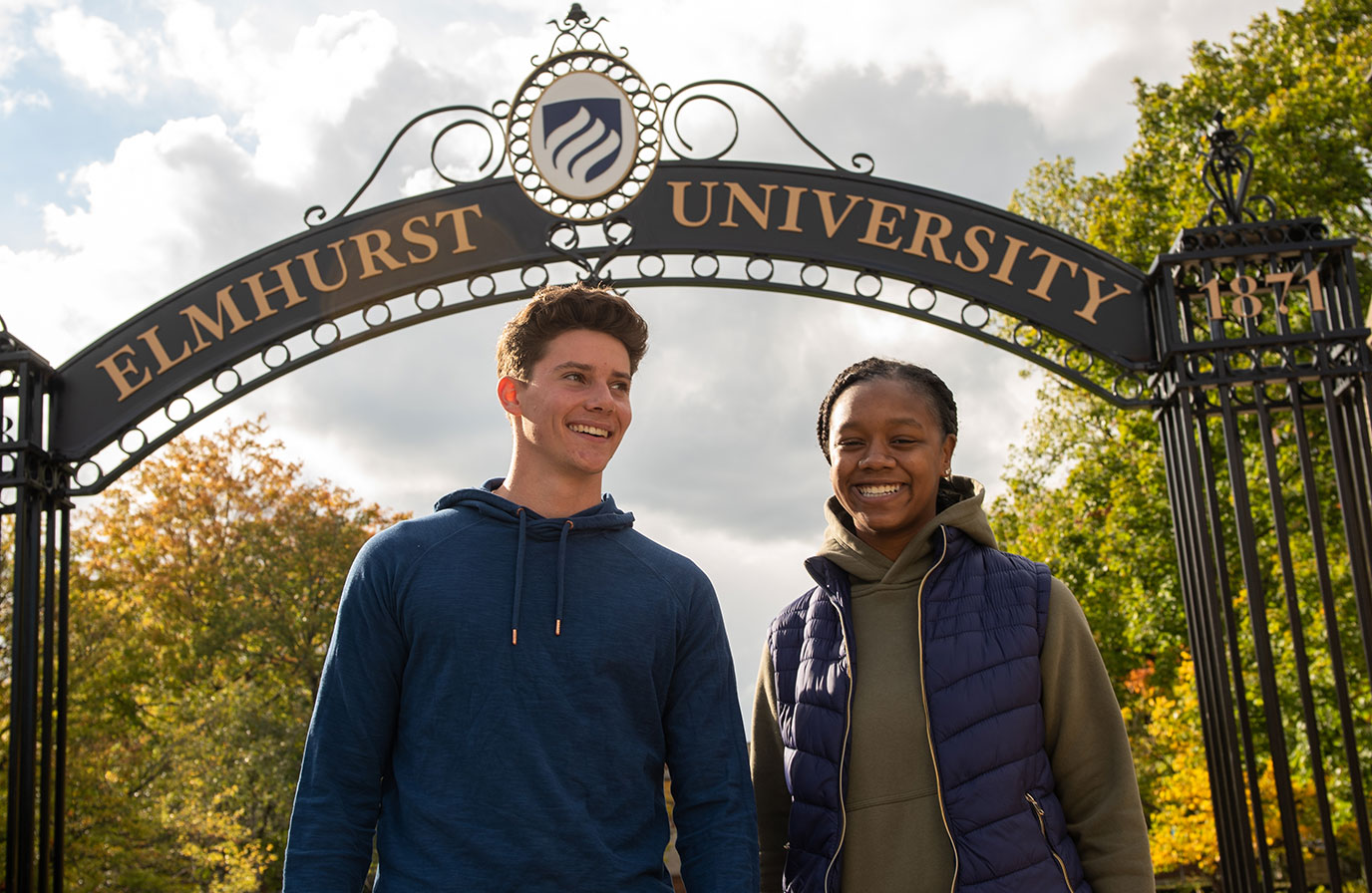 Two Elmhurst University 幸运艇 students, one male, one female, smile underneath the campus Gates of Knowledge.