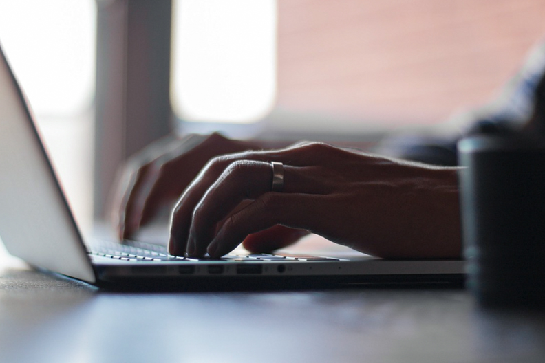 A person is shown typing on a laptop as part of coursework in digital marketing communication.