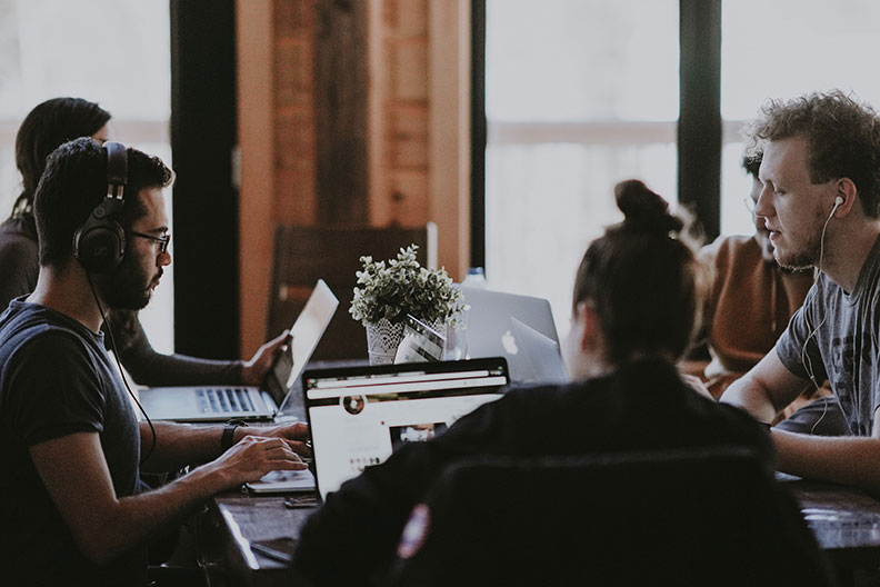A group of coworkers seated around a table looking at their laptops.