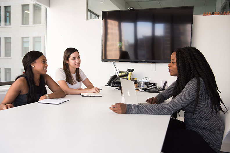 Three female employees sitting across from each other at a white table in an office.