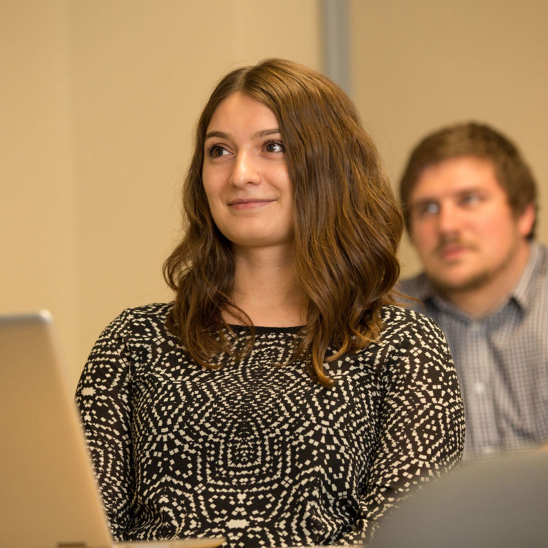 A female student, with a male classmate in the background, listens to a lecture during a marketing research graduate-level course at Elmhurst University.