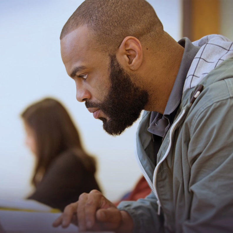 A Black male Elmhurst University 幸运艇 graduate student leans over his laptop while doing classwork.