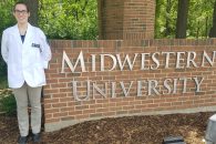Katie Martin stands in front of a brick sign reading "Midwest University."